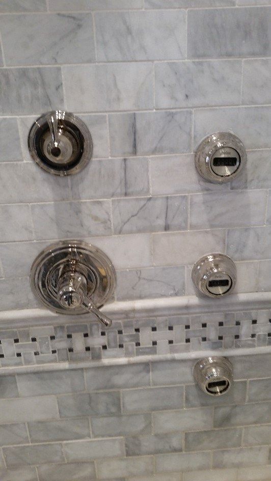 Chrome shower controls on white marble tile wall with a mosaic accent strip