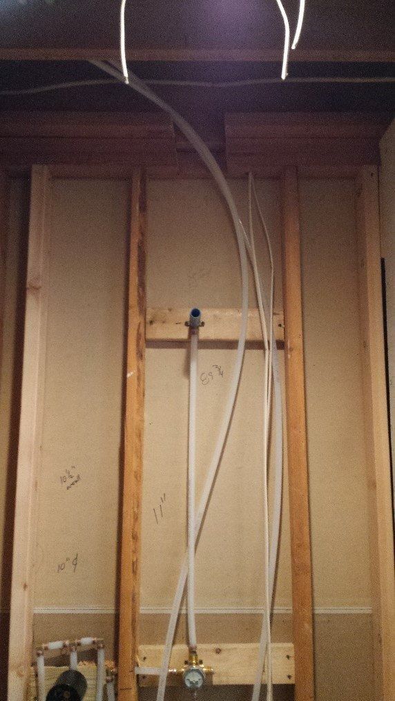 Exposed wall framing with plumbing pipes and a shower valve in a construction area