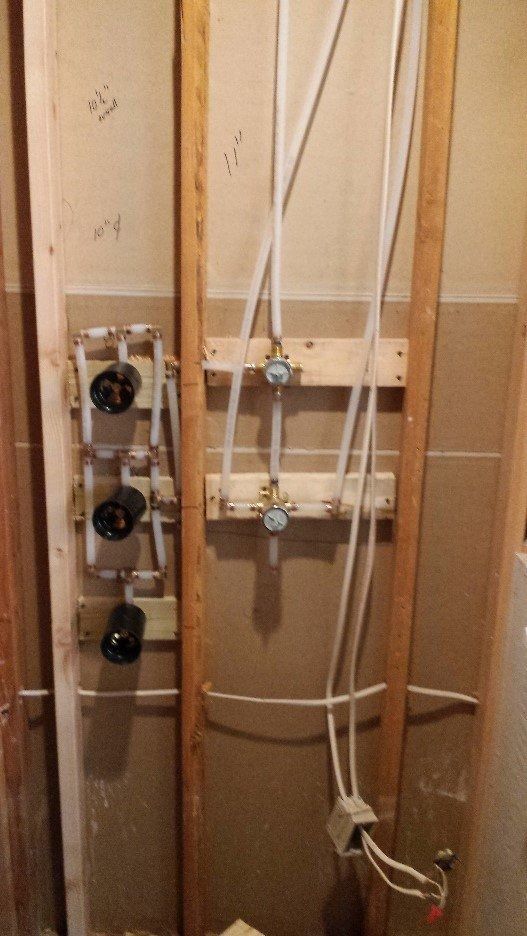 Exposed plumbing and valves inside an unfinished wall with pipes and fittings visible