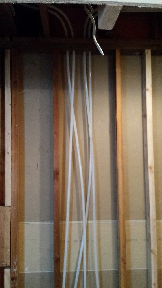 Exposed wall studs with several white and gray cables running vertically through an unfinished interior wall