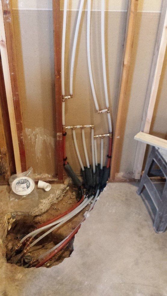 Open wall showing exposed plumbing pipes and wiring beside a concrete floor and unfinished room corner