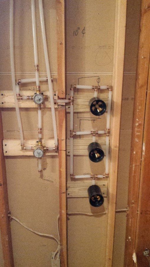 Plumbing pipes and valves mounted on a beige unfinished wall next to a wooden door frame