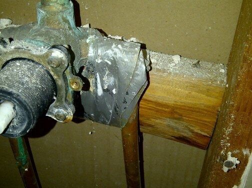Broken pipe clamp on a wooden beam with water damage and rust stains