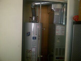Two large metal furnaces with silver ducts in a small utility closet
