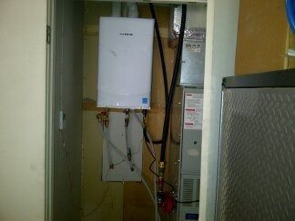 Wall-mounted boiler and utility equipment in a narrow closet, with pipes and cables visible.