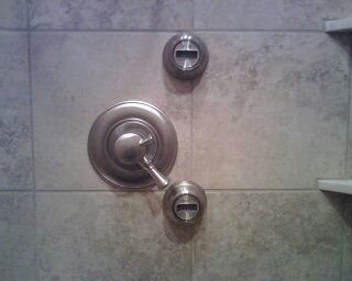 Shower wall with chrome temperature control and two valves on beige tile.