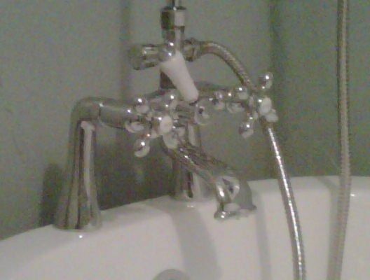 Bathtub faucet with a shiny chrome extender and clear bubble-like beads hanging over the tub.