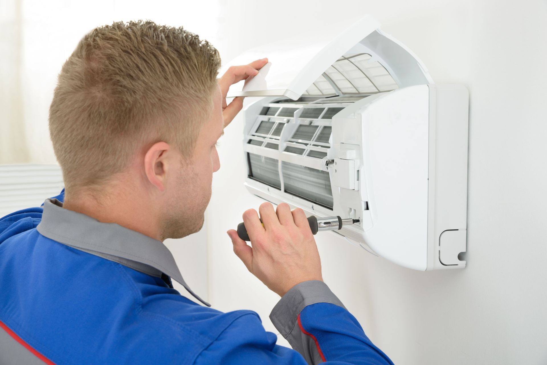 Technician inspecting a wall-mounted air conditioner unit with the front cover open