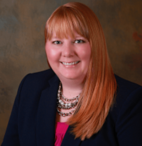 Studio portrait of a smiling woman in a dark blazer and pink top with layered necklaces