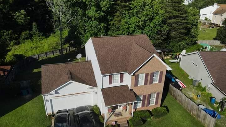 An aerial view of a two-story house with a brown roof and brown and white exterior, surrounded by trees and a few other houses.