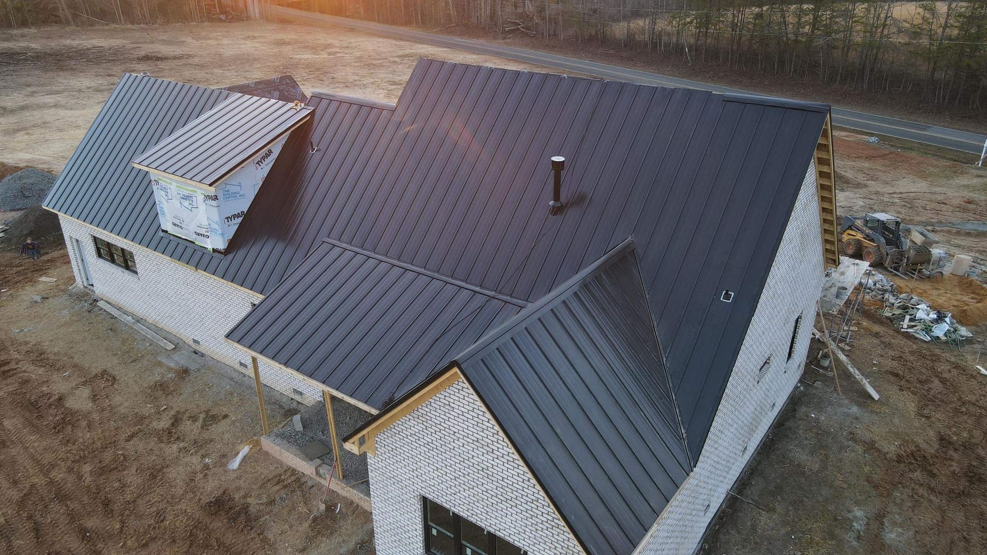 Black metal roof on a new house under construction; wood siding, porch, and a chimney.
