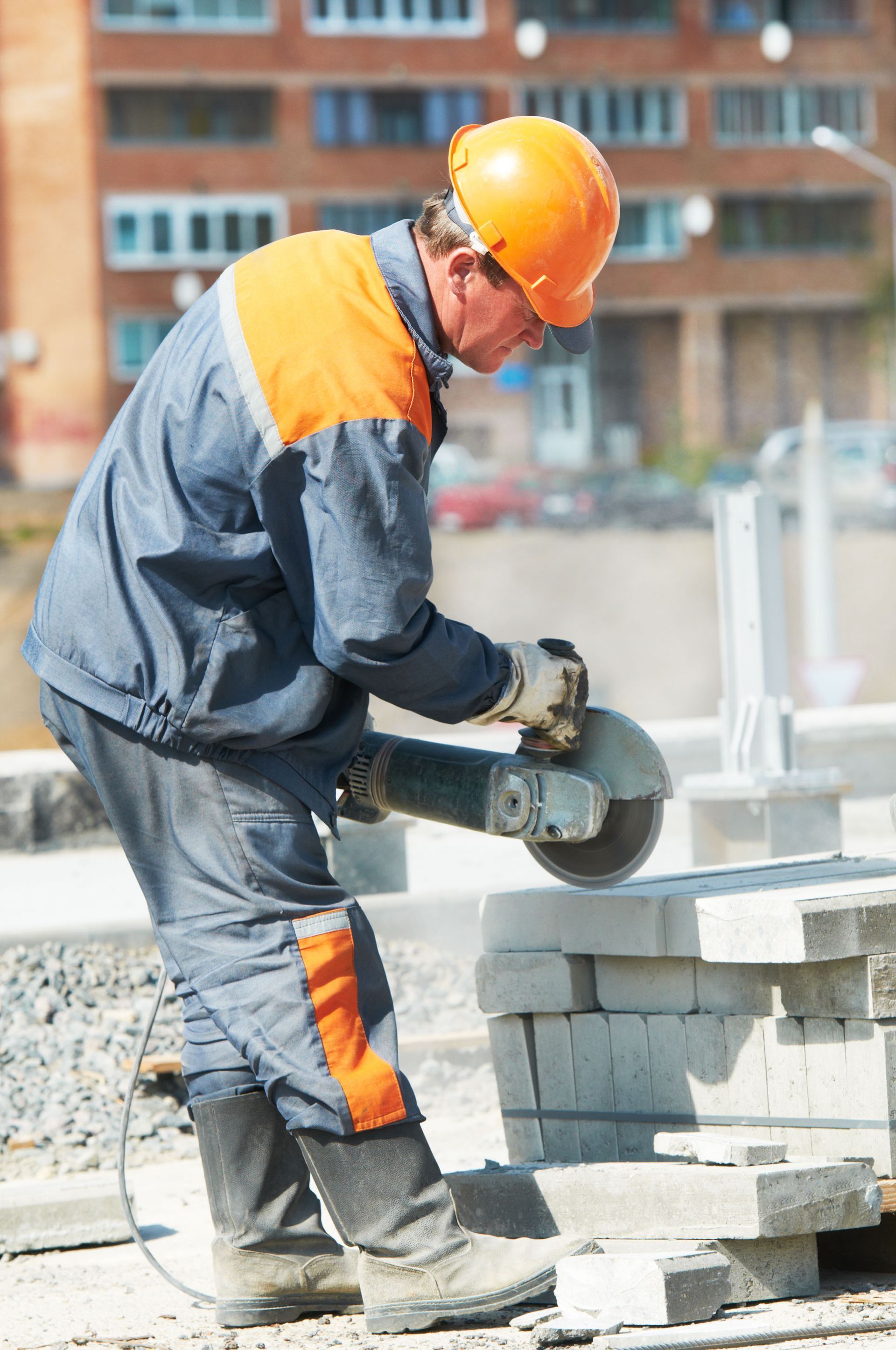 Construction worker in orange helmet cutting concrete blocks with a power saw outdoors