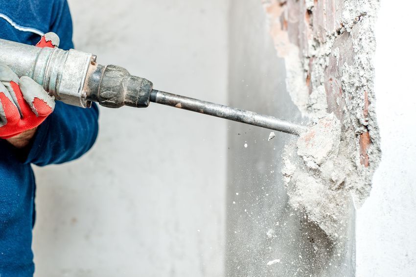 Worker using a jackhammer to chip away concrete from a wall indoors