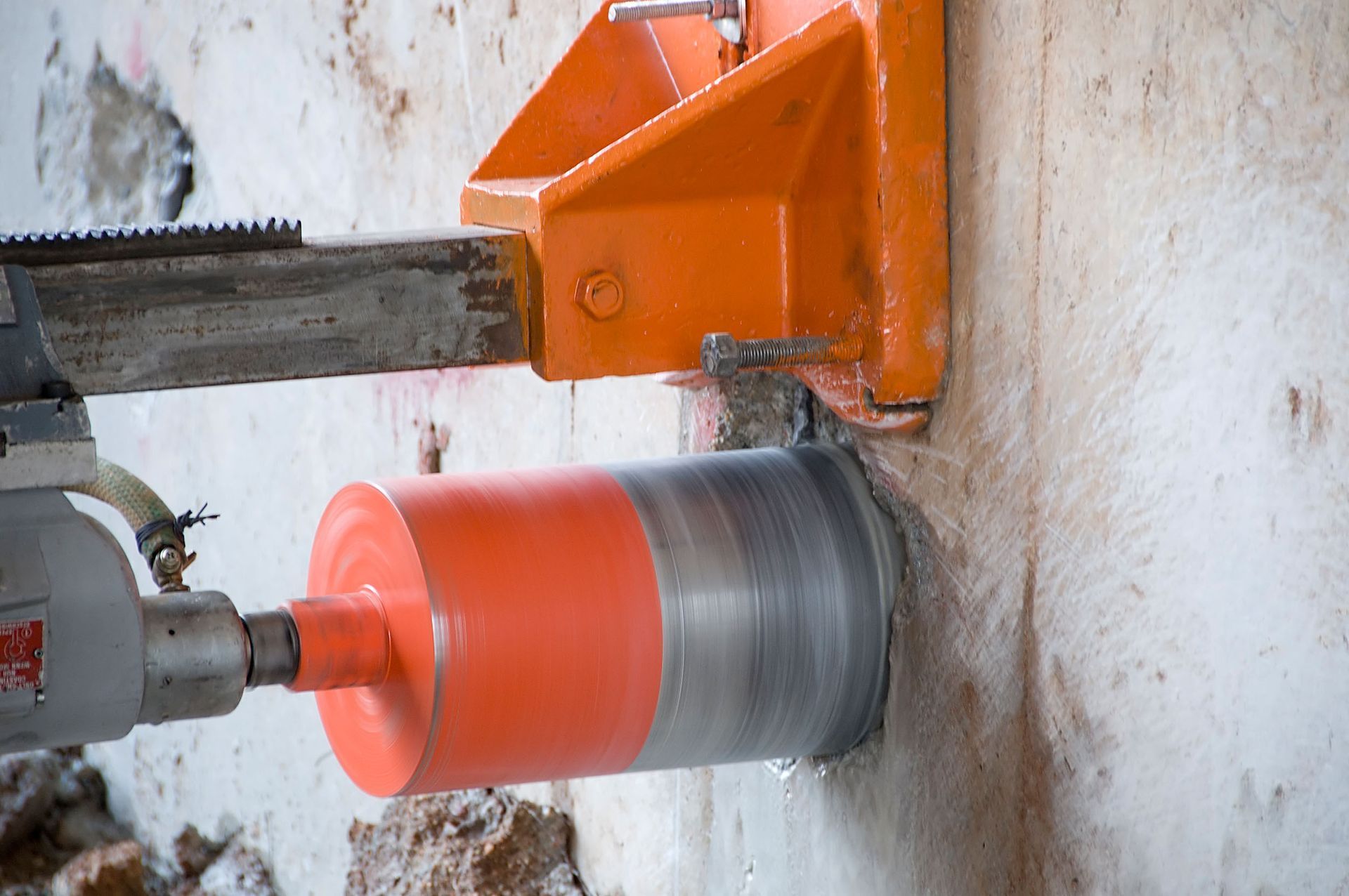 Diamond core drill bit cutting into a white wall with orange mounting hardware