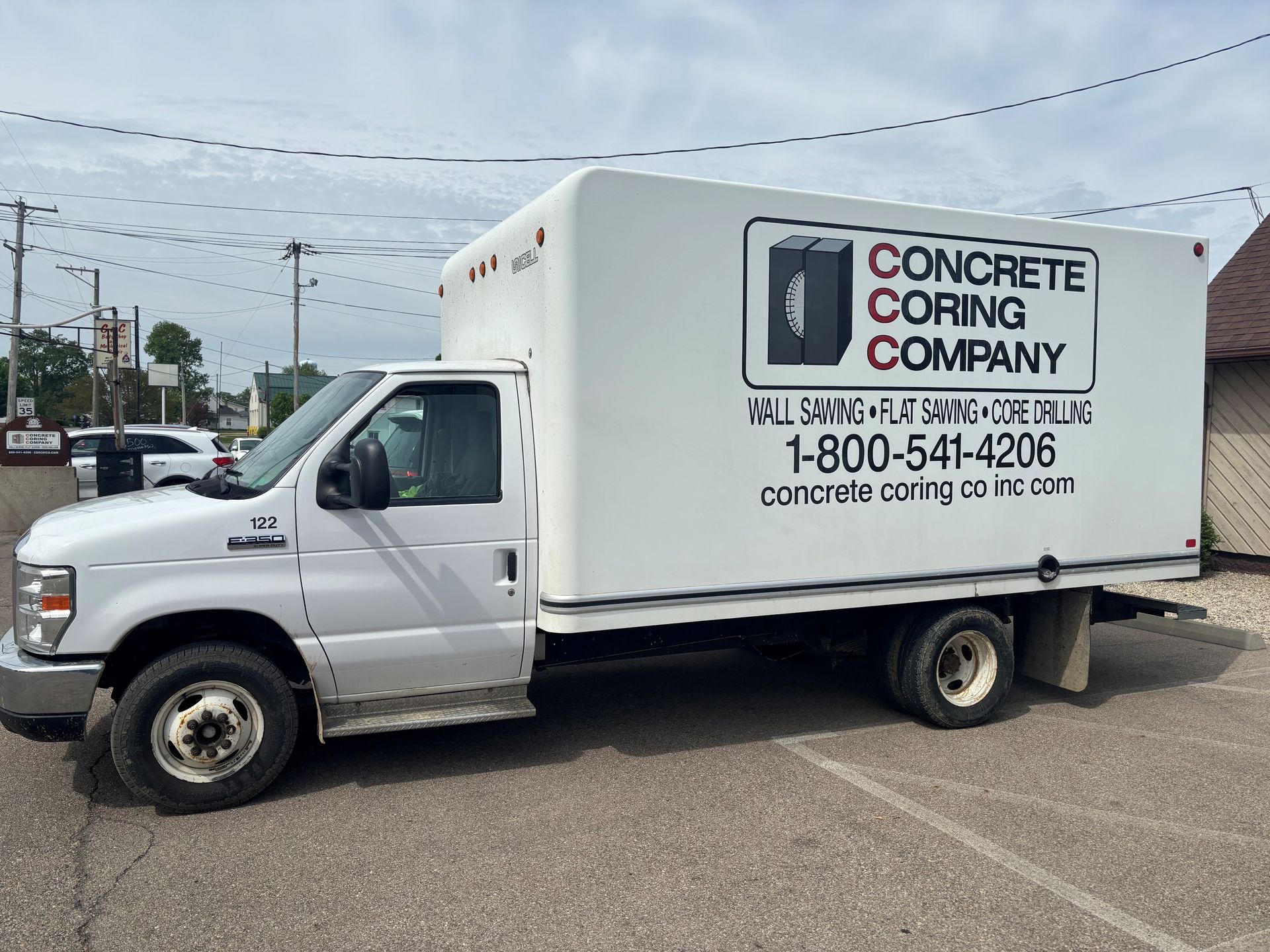 White Concrete Grinding Company box truck parked on a street under cloudy skies