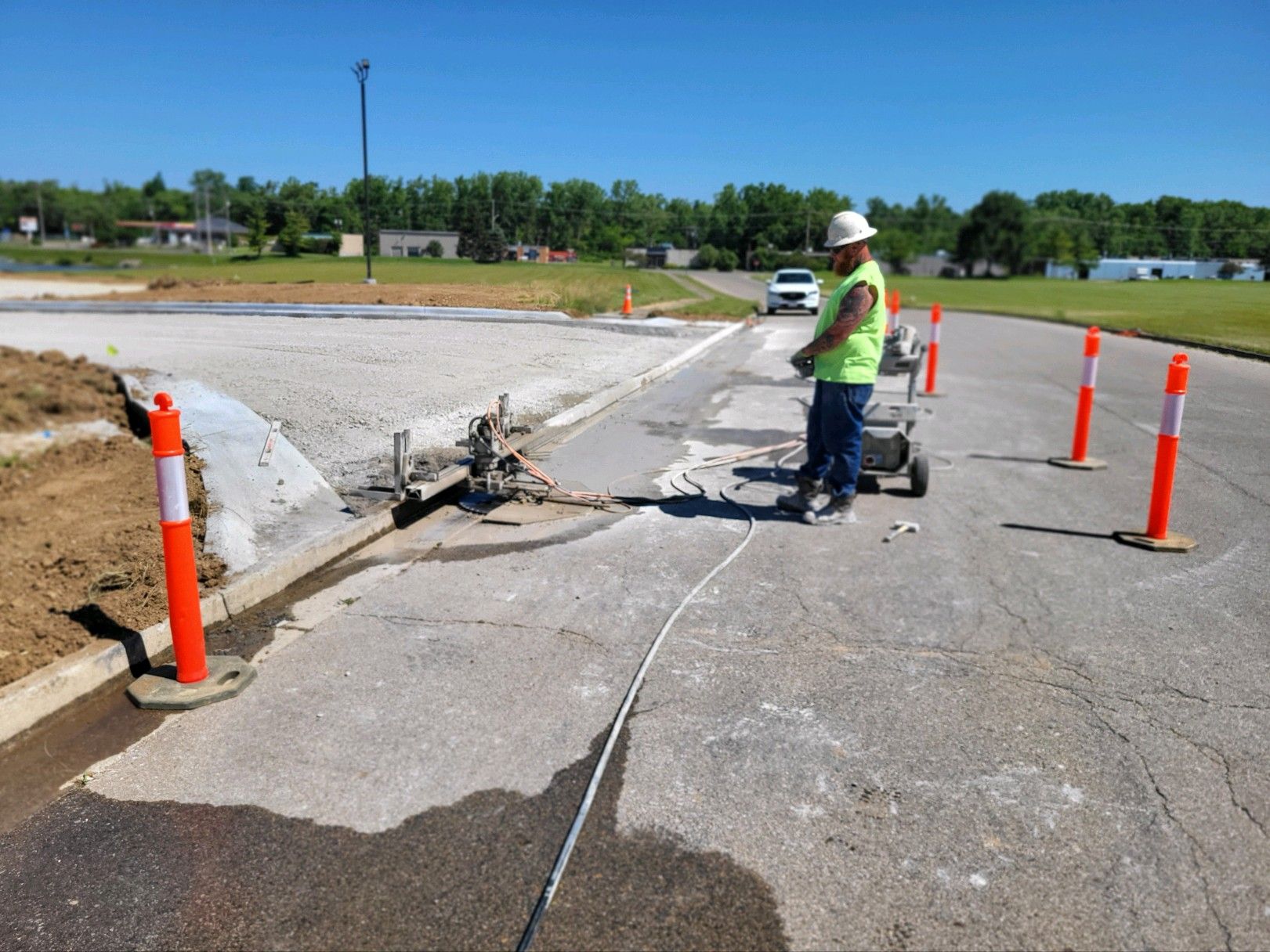 Road repair worker inspecting damaged pavement beside orange traffic cones on a cracked roadway