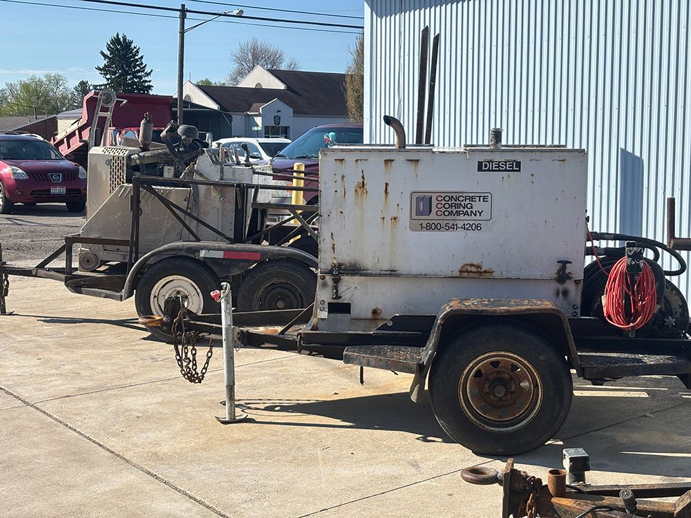 Trailer-mounted industrial equipment parked beside a metal building on a sunny day.