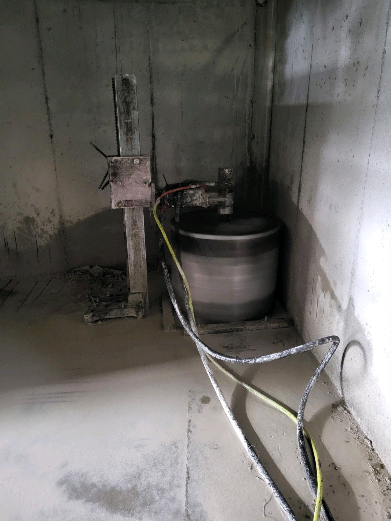 Industrial room with a metal tank, pipes, and cables beside a concrete wall.