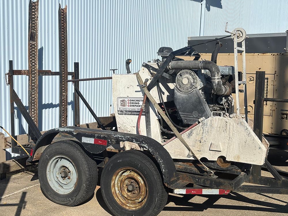 Small white skid steer on a trailer beside metal fencing and industrial equipment.