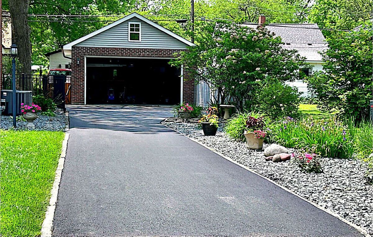 An asphalt driveway that leads to a garage with a house in the background