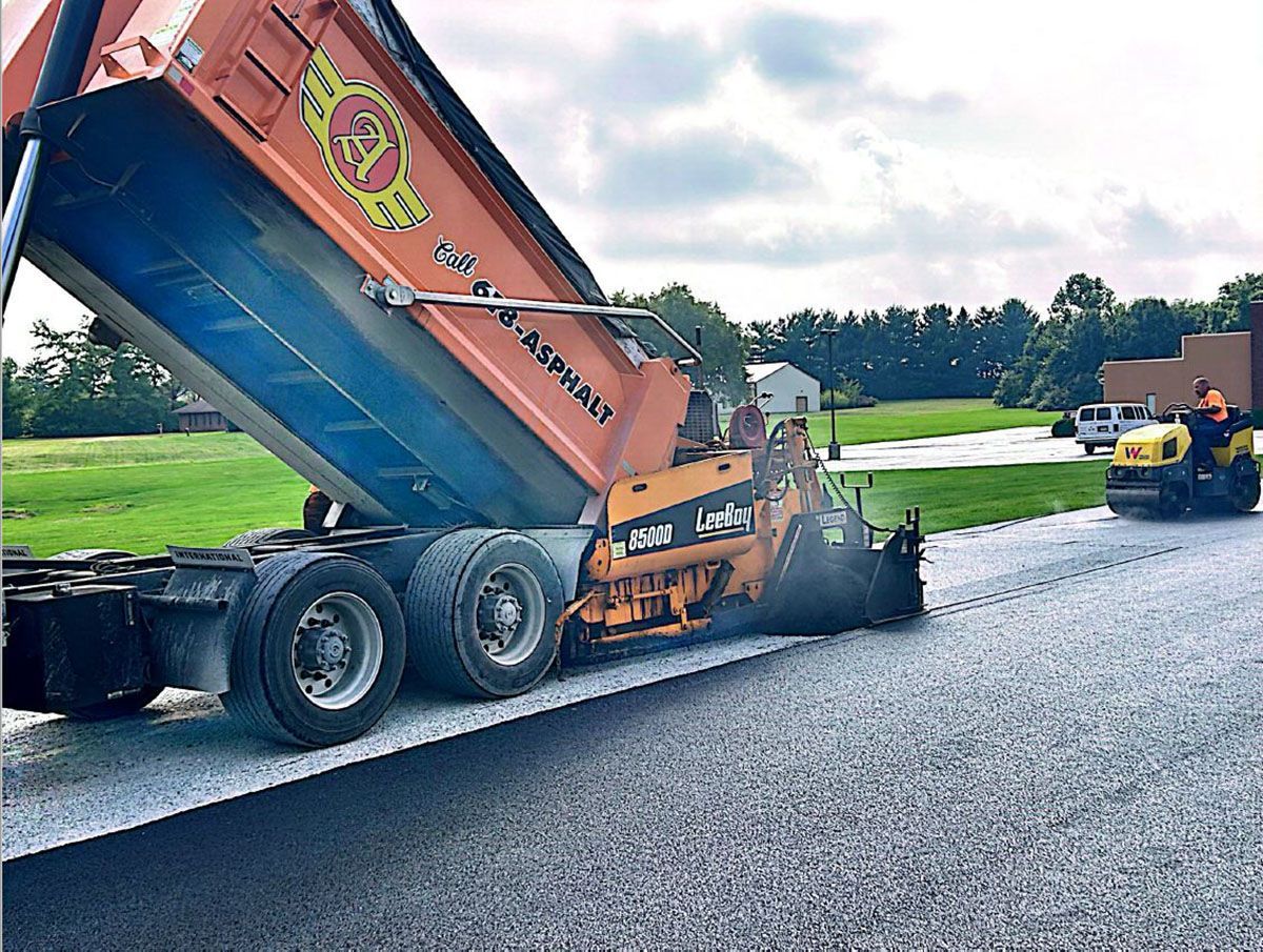 A dump truck pouring asphalt on a road