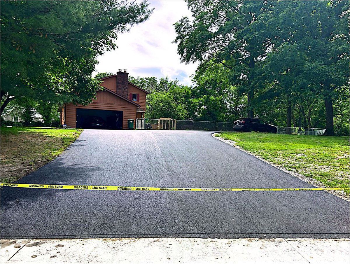 A newly paved driveway that leads to a house surrounded by trees