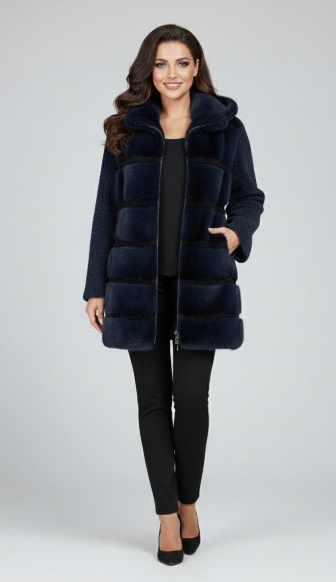 Woman in navy fur coat with hood, black pants, and heels. Smiling, standing in a studio setting.