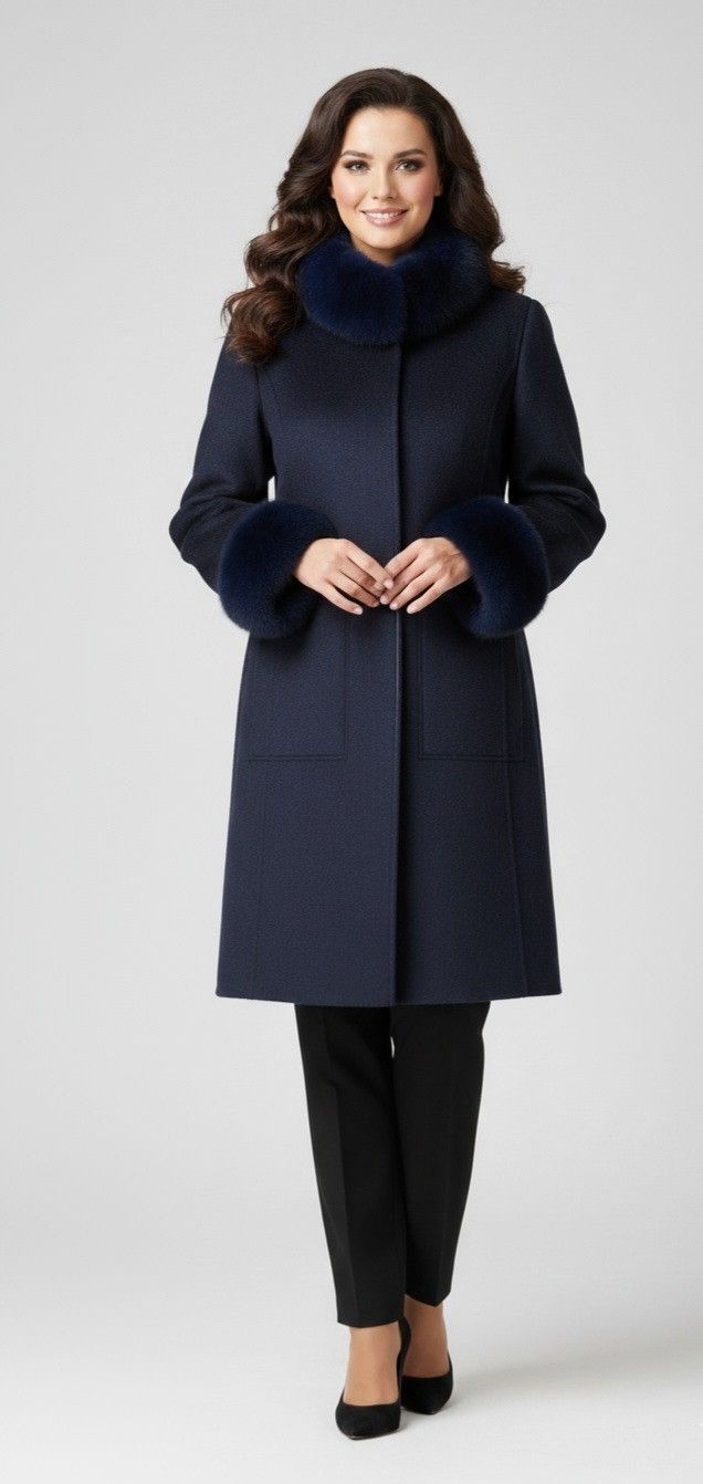 Woman wearing a navy coat with fur collar and cuffs, black pants, and heels against a white backdrop.