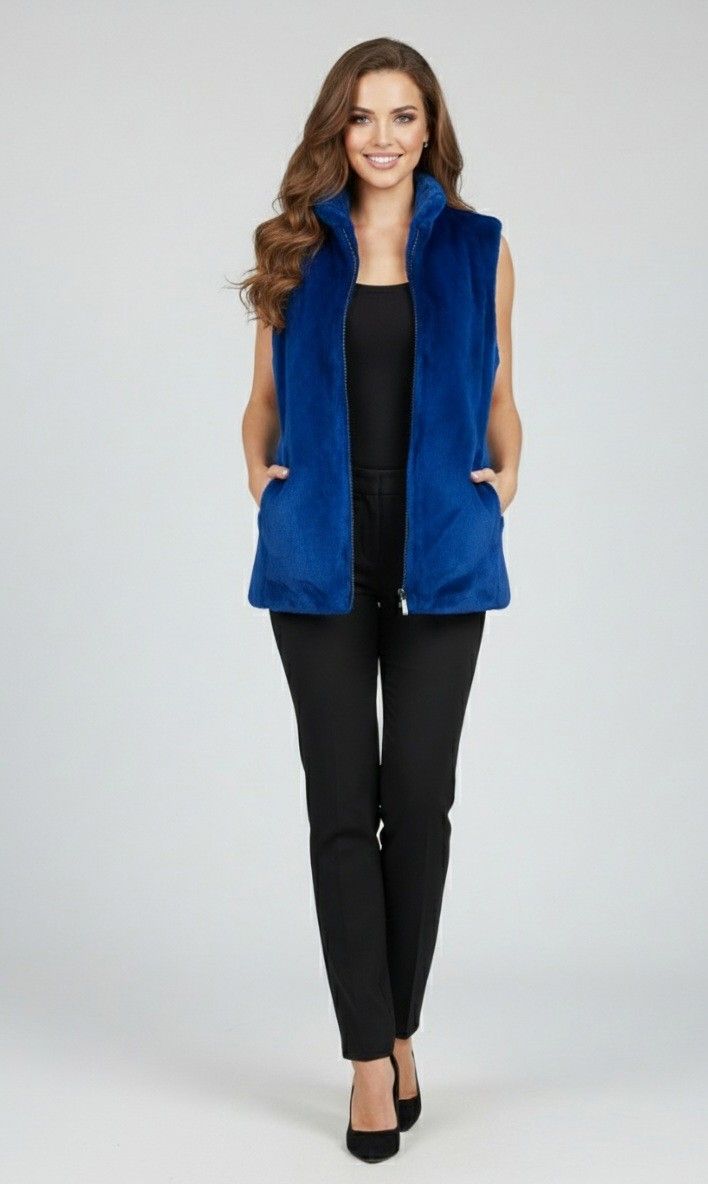 Woman in a blue fur vest, black top and pants, smiling, hands in pockets.