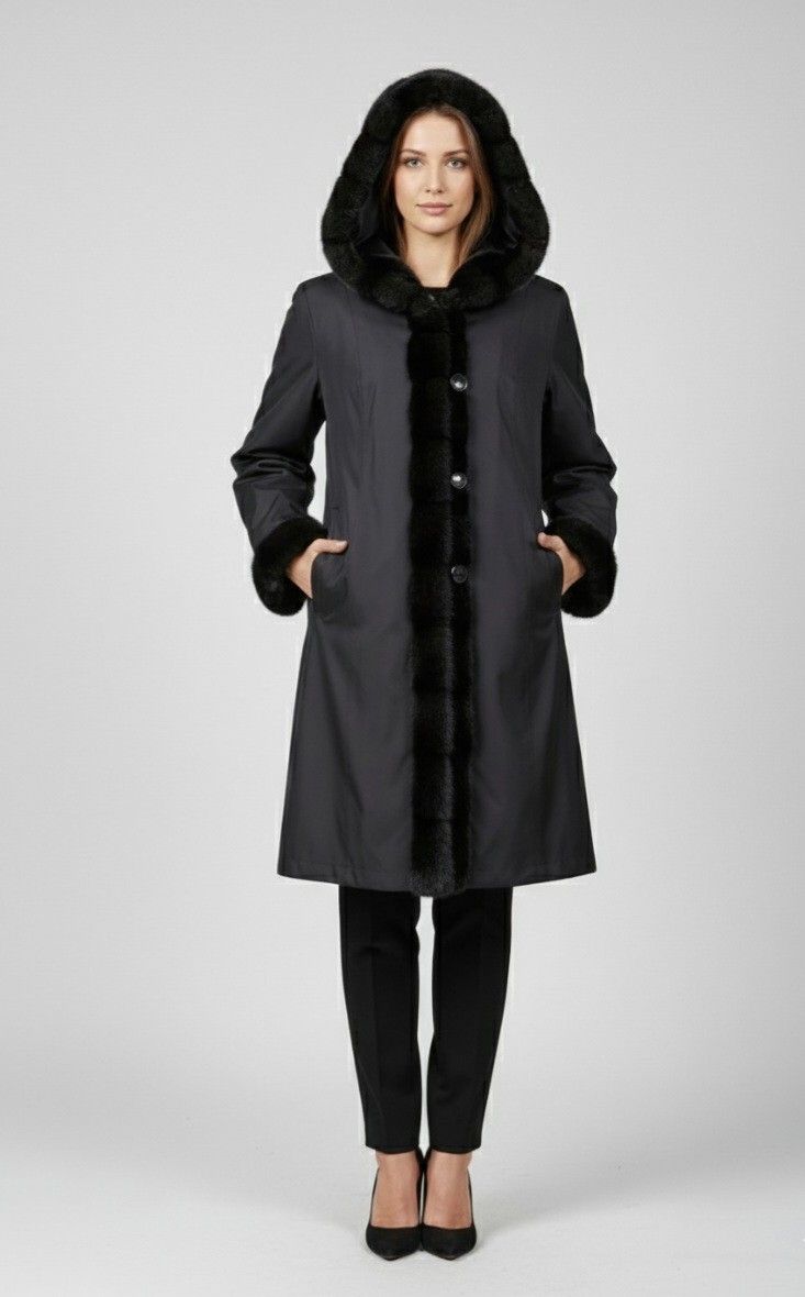 Woman in a dark coat with a fur-trimmed hood, cuffs, and front panel, standing against a light background.