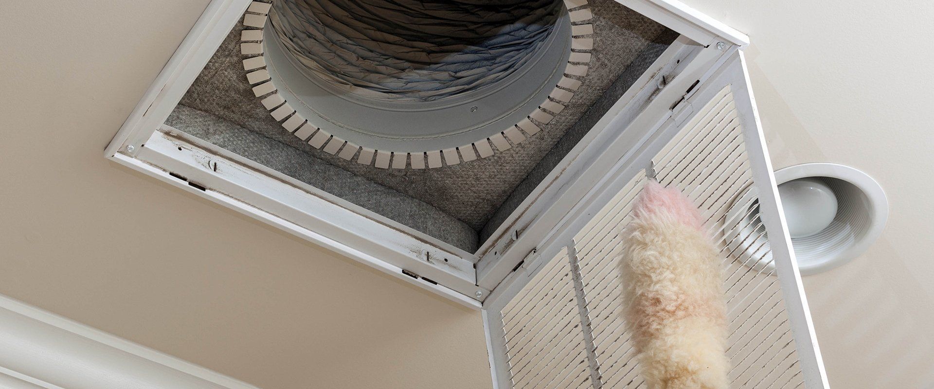 A person is cleaning an air vent with a duster
