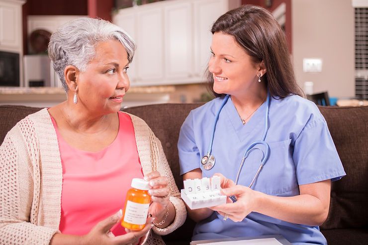 A nurse is giving an elderly woman a bottle of pills.