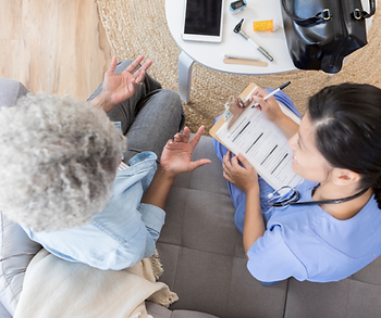 A nurse is talking to an elderly woman on a couch.