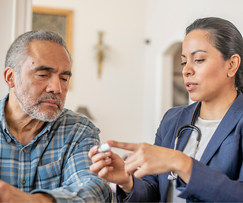 A female doctor is talking to an older man who is holding a pill.