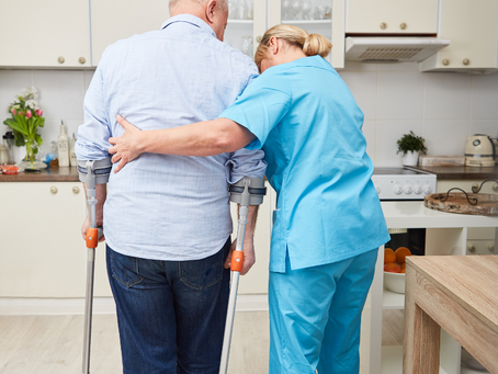 A nurse is helping a man with crutches walk in the kitchen.