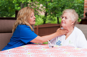 A nurse is helping an elderly woman with her throat while sitting at a table.