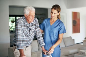 A nurse is helping an elderly man walk with a walker.