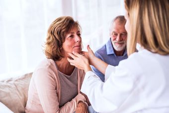 An elderly couple is sitting on a couch talking to a doctor.