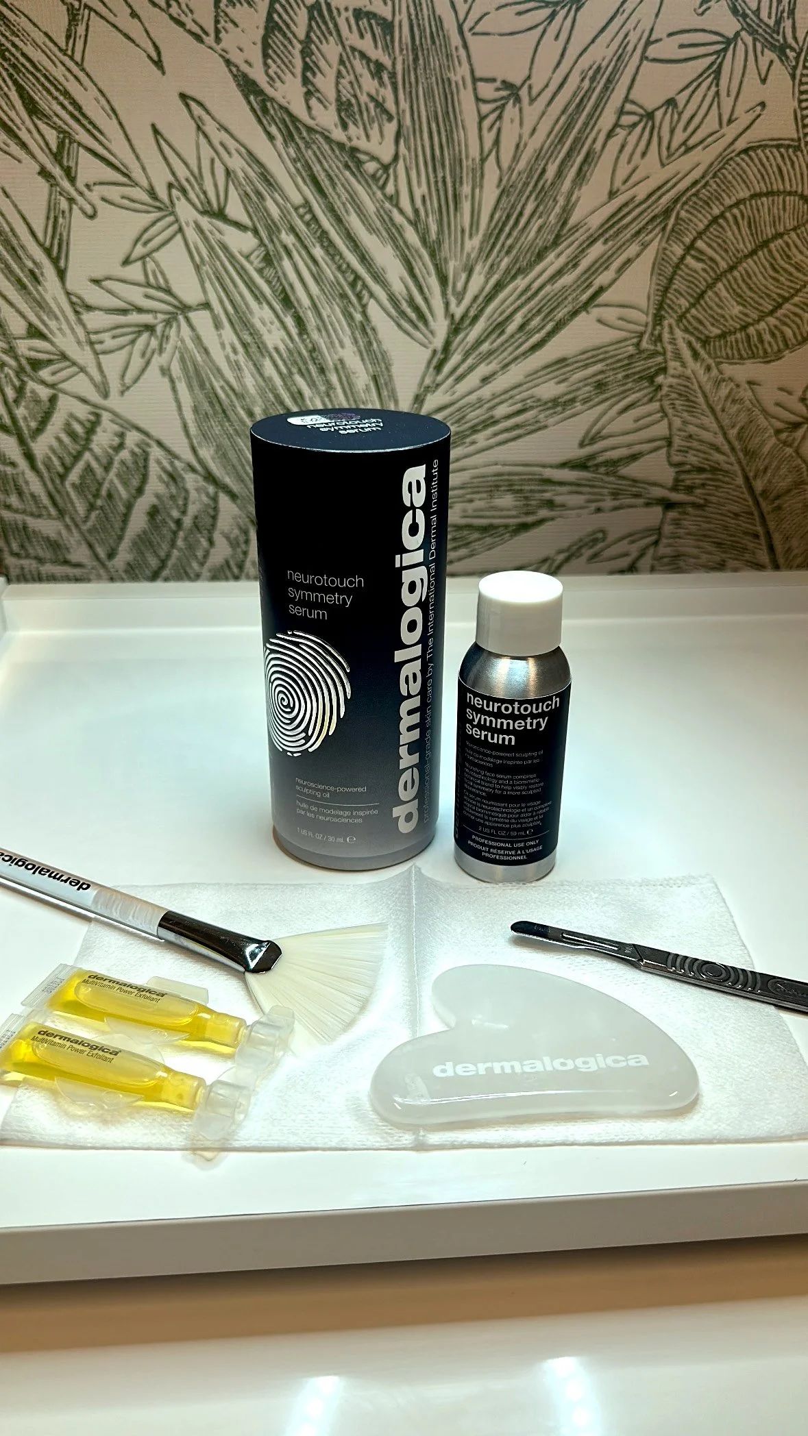Skincare products on a tray: Dermalogica cylinder, face oil, gua sha tool, needles and a pen.
