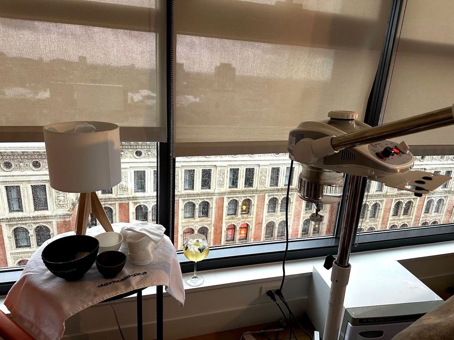 Spa setup with facial steamer and bowls on a table by a window overlooking a city.