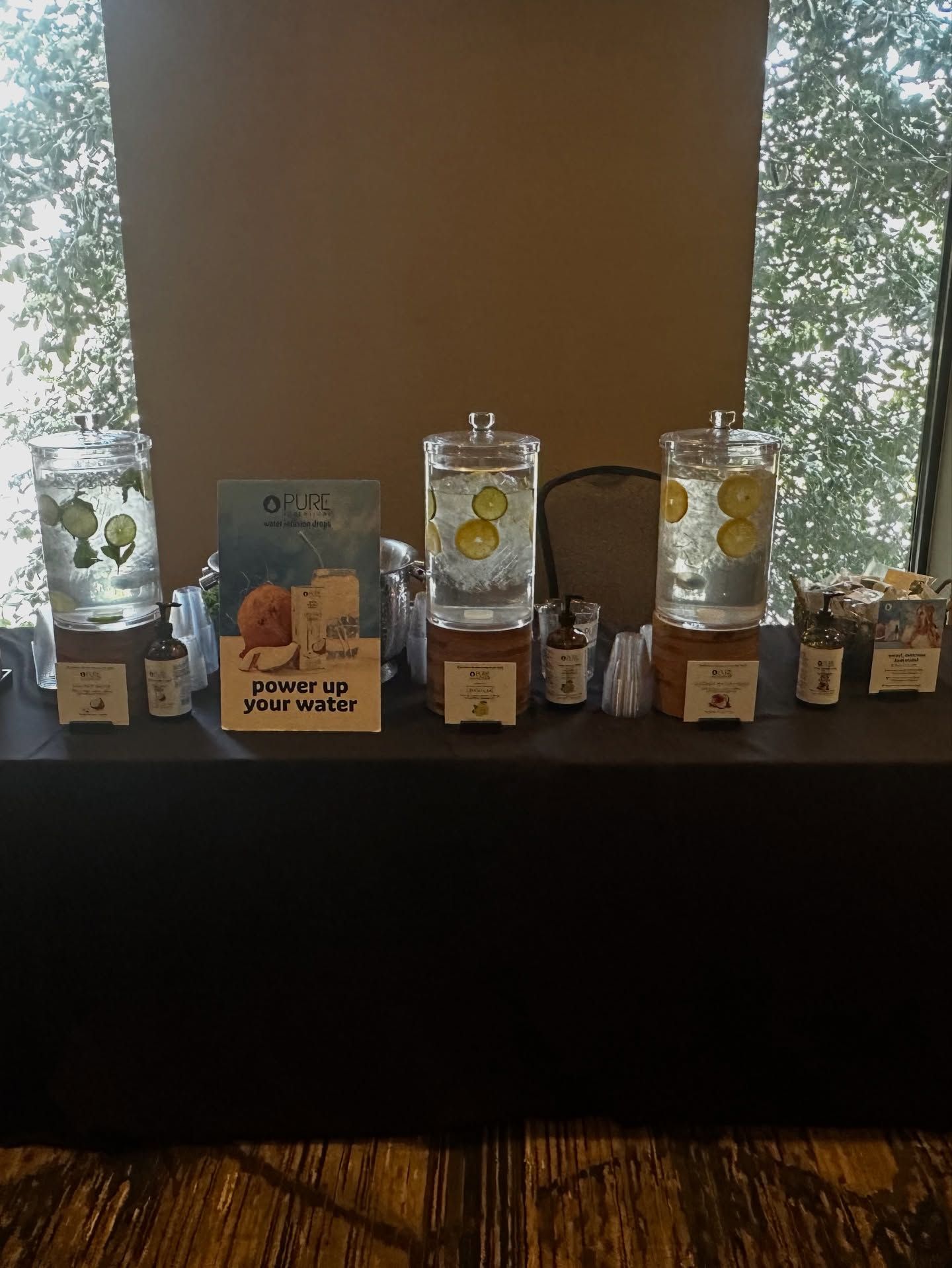 Three beverage dispensers on a table, each containing fruit-infused water. A sign describes the drinks.