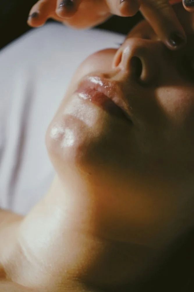 Close-up of a person's face tilted up, with hands above. Lips are glossy, skin glowing.