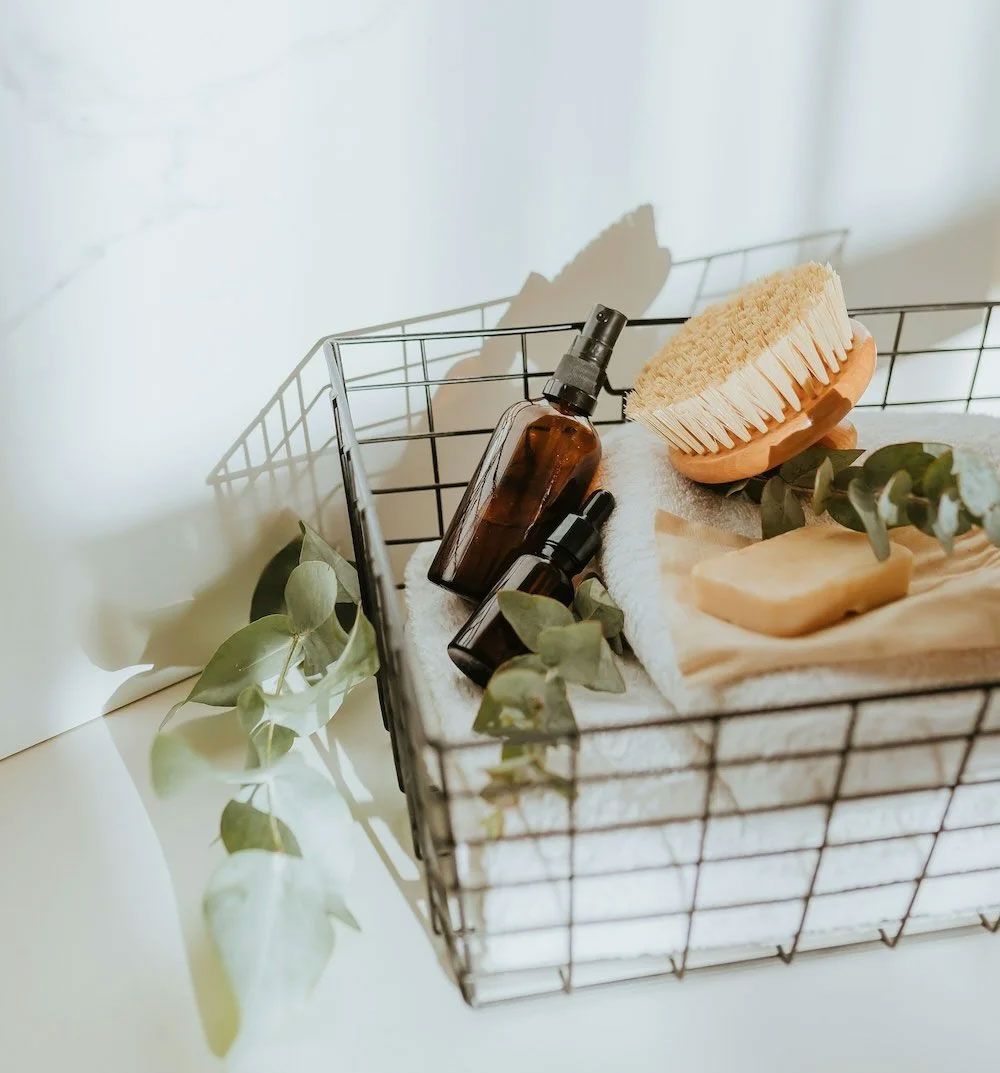 Wire basket with brown bottles, a brush, and soap on a towel.