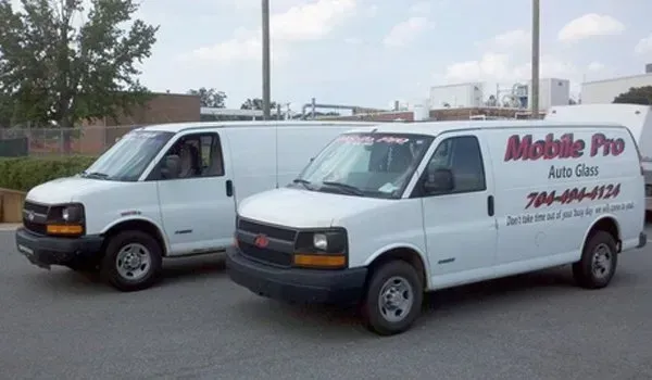 Two white Mobile Pro Auto Glass vans parked on pavement; one has the company logo.