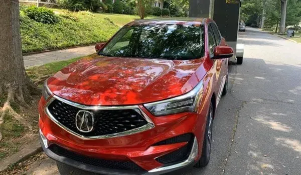 Red Acura RDX SUV parked on a tree-lined street, towing a small trailer.