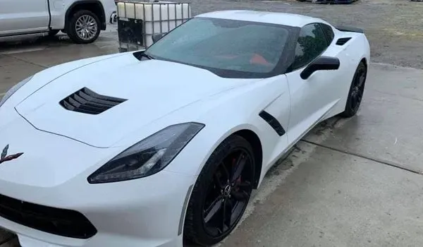 White Corvette sports car with black accents, parked on a wet surface.