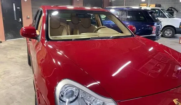 Red Porsche Cayenne SUV parked in a garage with tan interior and other vehicles visible.