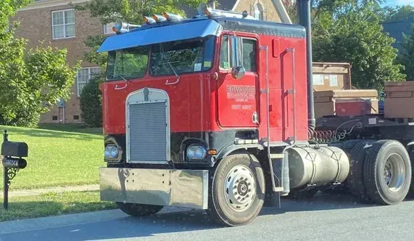 Red Kenworth semi-truck parked on a residential street. Chrome bumper, blue sun visor, mailbox in view.
