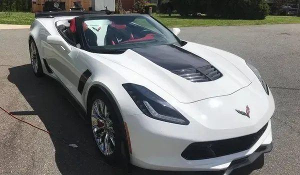 White convertible Corvette with black hood parked outdoors.