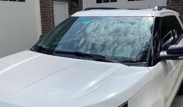 White SUV with a foamy windshield reflecting the sky. Parked in front of a brick building.